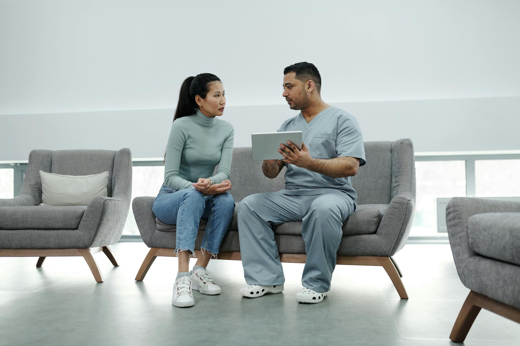 A clinician engaging with an Asian patient over a tablet in a modern clinic